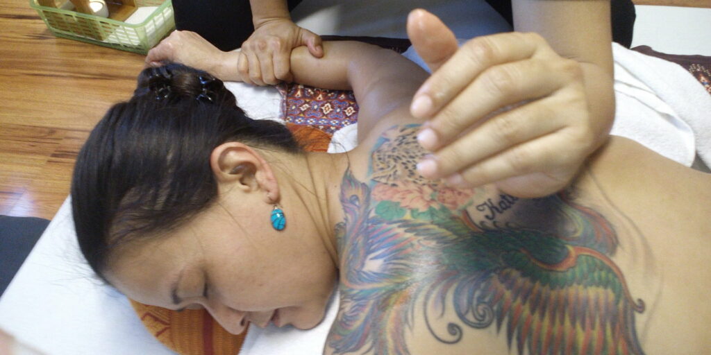 Rückenmassagetechnik der traditionellen Thai Massage bei einer Frau mit Tätowierungen.