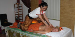 Eine Thai Masseurin kniet über eine rblonden Frau und massiert sie.