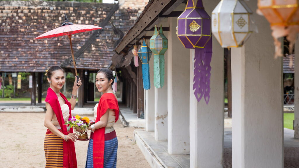 Zwei junge Thailänderinnen in einem Tempel mit einem Sonnenschirm.