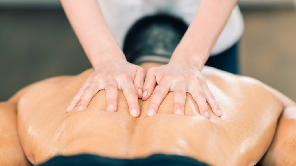 Zwei Hände auf dem nackten Rücken eines Mannes, bei dem mit einer Thai Massagetechnik Verspannungen wegmassiert werden.