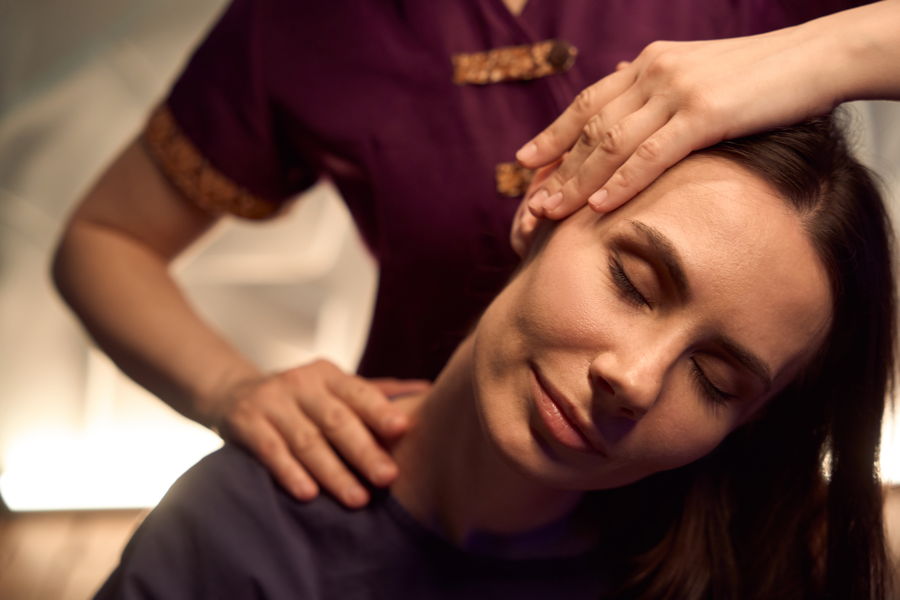 Ein dunkelhaarige Frau mit geschlossenen Augen und entspanntem Gesichtsausdruck geniesst eine Thai Massage, nachdem sie sich darauf vorbereitet hat.